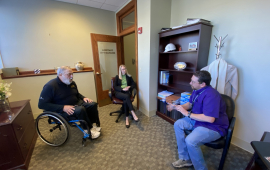 Man in wheelchair visits city staff inside city offices to talk about accessibility issues.