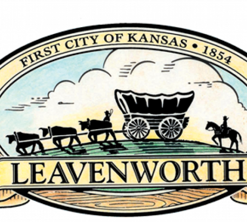 Logo of Leavenworth shows a covered wagon and set of cattle pointing left in in front of green grass and blue sky.