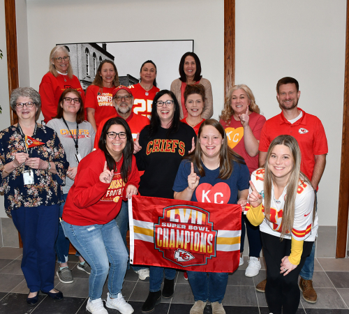 City staff wearing their favorite football team, Kansas City Chiefs gear and carrying a flag inside a building