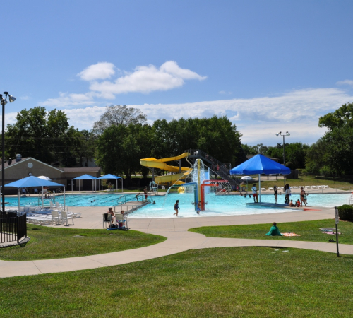 photo of pool with zero depth entry surrounded by green grass and sidewalks