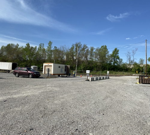 Entrance to the Leavenworth Brush Site, several piles of brush and yard waste on a gravel lot with a trailer office and vehicles