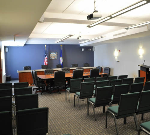 Photo of Commission room with chairs for the public, a podium for the public in front of a desk for elected officials