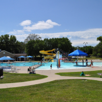 photo of pool with zero depth entry surrounded by green grass and sidewalks