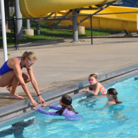 children in pool look at young woman bending into pool to teach