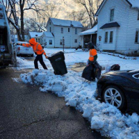 City crews in orange reflective jackets carrying trash bags through deep snow