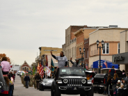 Parade through downtown street with two African - American men standing on float waving to crowd