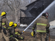 Firefighters with a water hose in front of a burning house