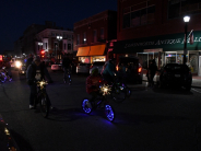 Bicycles outlined with strings of holiday lights shine while riding down a dark street