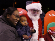 A woman and a young child smile at a camera next to a man in a red hat and coat dressed as Santa