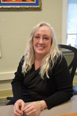 Photo of woman sitting at desk with blonde hair, glasses and a black sweater