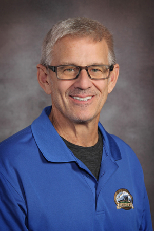 Photo of man with short gray hair and glasses wearing a blue polo shirt