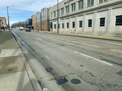 Photo of street next to buildings. The street shows patching and wear and tear.