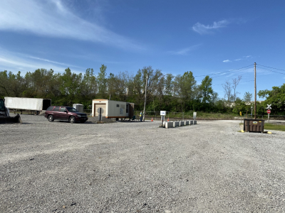 Entrance to the Leavenworth Brush Site, several piles of brush and yard waste on a gravel lot with a trailer office and vehicles