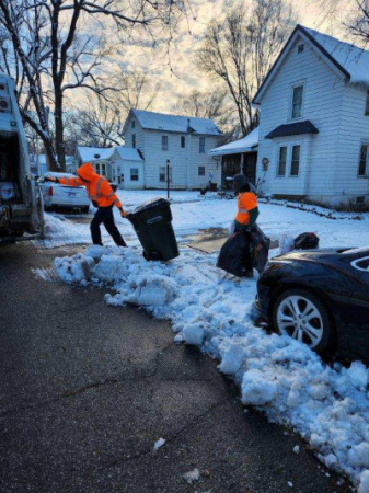 City crews in orange reflective jackets carrying trash bags through deep snow