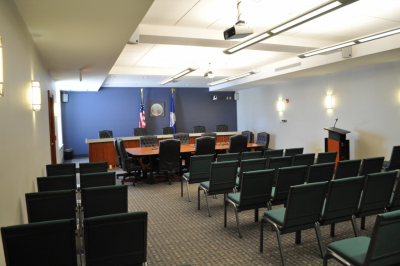 Photo of Commission room with chairs for the public, a podium for the public in front of a desk for elected officials