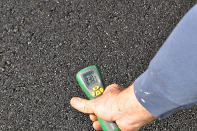 Digital readout of thermometer on recently paved asphalt shows 230.7 degrees Fahrenheit