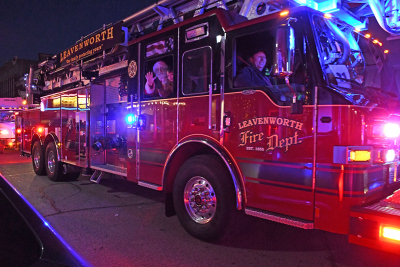 Santa and small child wave from the seat of a large fire truck lit up at night