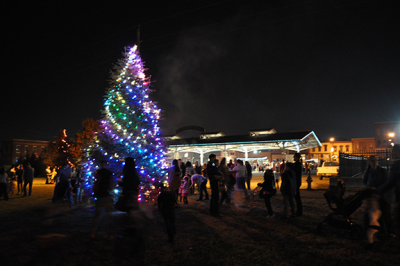 lit evergreen tree at night with purple, white, blue and green lights and people standing around it in the dark