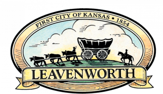 Logo of Leavenworth shows a covered wagon and set of cattle pointing left in in front of green grass and blue sky.