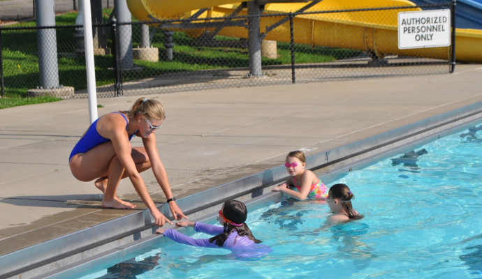 children in pool look at young woman bending into pool to teach